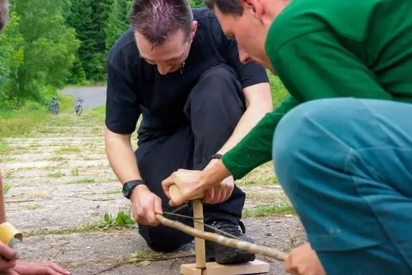 Zwei Personen bauen eine Schlagfalle (Figure-Four) aus Holzstücken