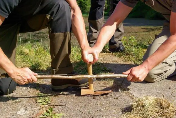Zwei Personen nutzen eine Feuerbohrmaschine mit Holzstück und Schnur