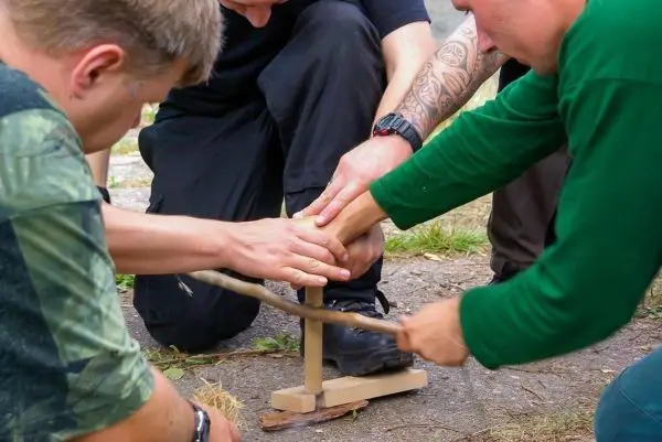 Zwei Personen nutzen eine Feuerbohrmaschine zur Zundererzeugung