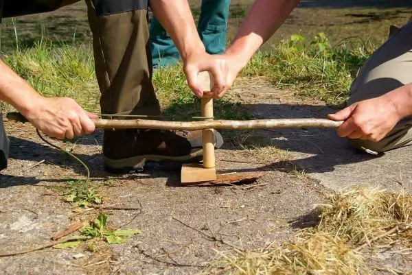 Zwei Personen nutzen eine Holzbohrmaschine, um ein Loch in ein Stück Holz zu bohren