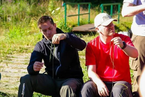 Zwei Personen sitzen im Gras und halten Gräser in den Händen