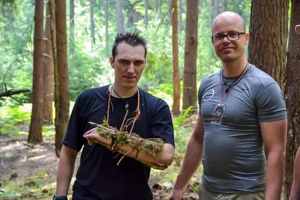 Zwei Personen stehen im Wald, einer hält ein Bündel mit Moos und Ästen
