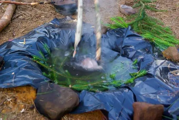 Zwei Stöcke halten einen Behälter über dampfendes Wasser im Freien