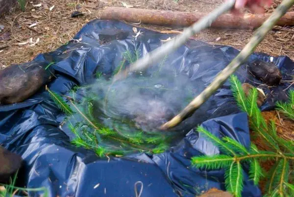 Zwei Stöcke rühren Wasser in einer improvisierten Wassererhitzung mit Folie und Steinen