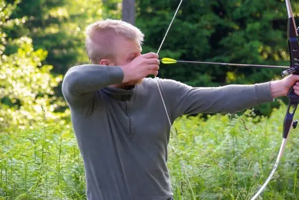 Bogen wird gespannt, Pfeil zielt auf ein Ziel im Grünen