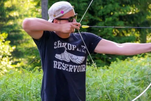 Bogen wird gespannt, Pfeil zielt auf ein Ziel im Hintergrund
