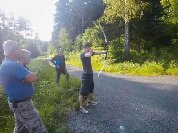 Bogen wird von einem Mann auf einem Schotterweg gespannt, Zuschauer beobachten