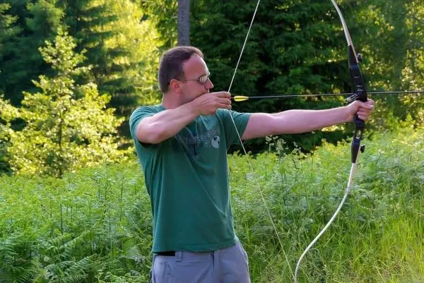 Bogenschütze spannt Pfeil in einem grünen Waldgebiet