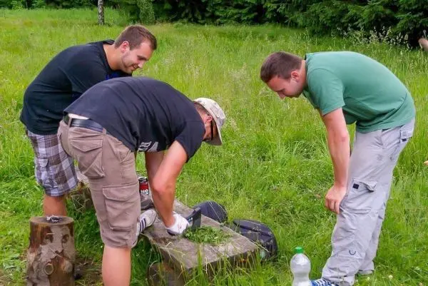 Drei Personen arbeiten an einem Holzstück, während sie Materialien auf einem Tisch anordnen