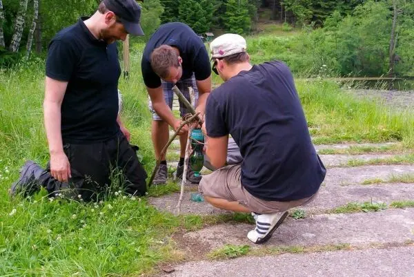 Drei Personen bauen eine selbstgebaute Konstruktion aus Ästen und Seil