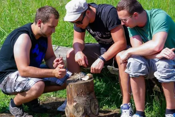 Drei Personen bearbeiten Zunder auf einem Baumstumpf im Freien
