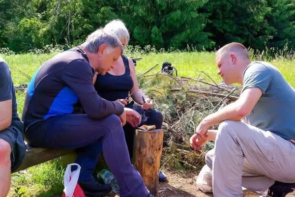 Drei Personen sitzen um einen Holzblock und bearbeiten mit einem Messer Holz
