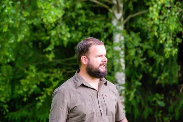 Ein Mann steht vor einer grünen, bewaldeten Kulisse