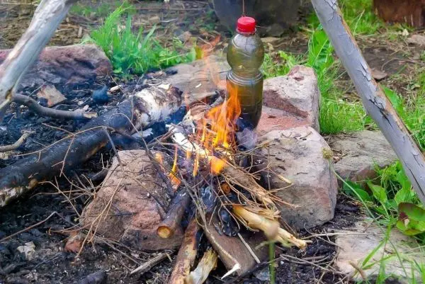 Feuer brennt zwischen Steinen mit einer Flasche daneben beim Überlebenstraining
