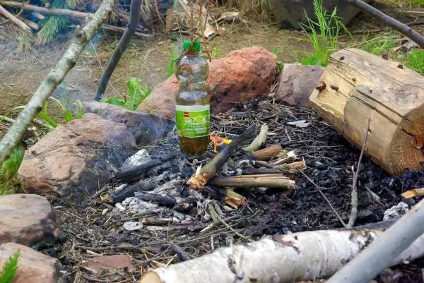 Flasche steht auf einem Feuerplatz mit Holz und Asche