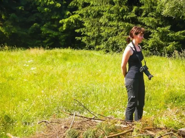 Frau steht auf einer Wiese neben einem Haufen Äste und beobachtet die Umgebung