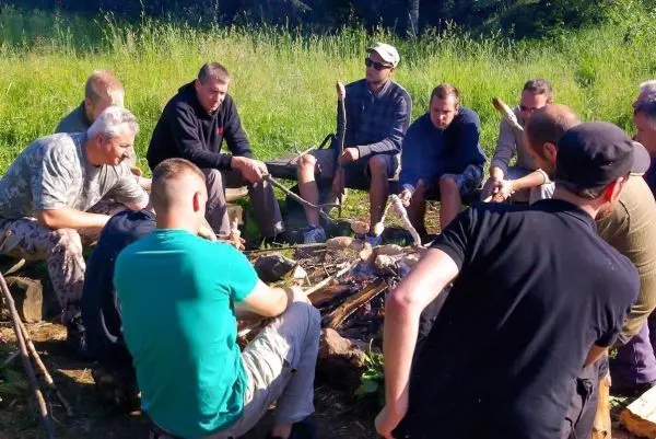 Gruppe sitzt um ein Feuer und bereitet mit Stöcken Essen zu