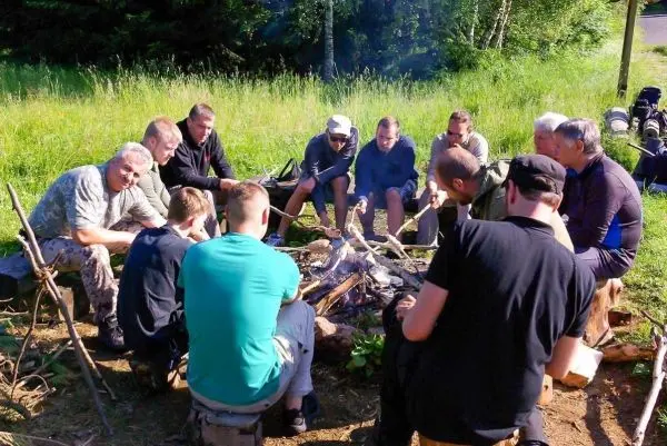 Gruppe sitzt um ein kleines Bodenfeuer und wärmt sich in der Natur