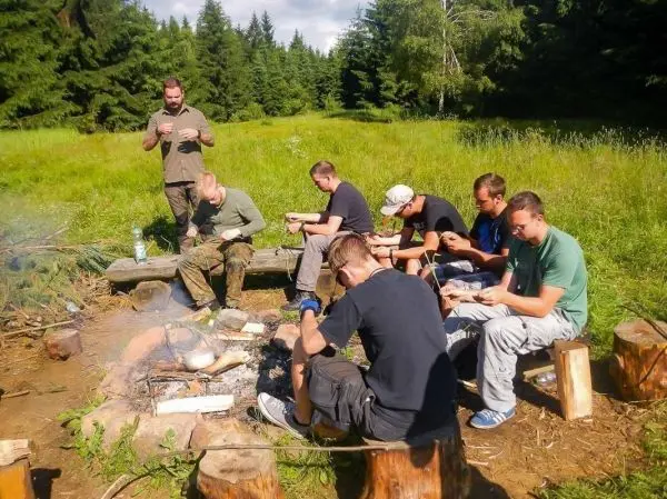Gruppe sitzt um ein Lagerfeuer und bereitet Zunder vor