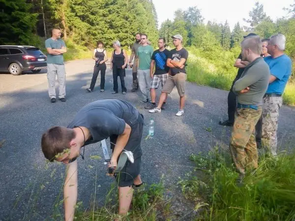 Gruppe steht auf einem Schotterweg, einer beugt sich nach vorne und untersucht den Boden