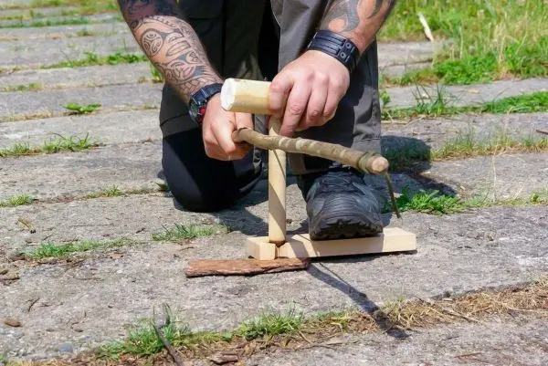 Holzstück wird mit einem Bohrer in einer selbstgebauten Feuerstelle bearbeitet