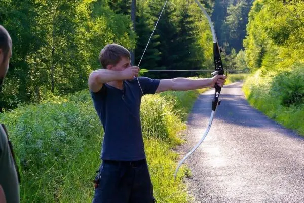 Junge spannt einen Bogen auf einem Waldweg