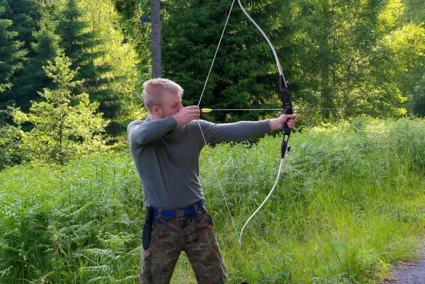 Junge spannt einen Bogen in einer bewaldeten Umgebung