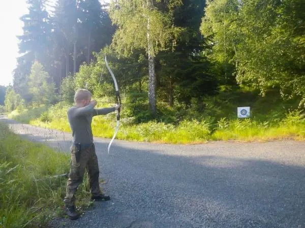 Junge spannt einen Bogen in Richtung Zielscheibe im Wald