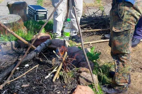 Kessel hängt über kleiner Flamme, umgeben von Steinen und Holz