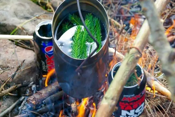 Kessel mit Wasser und Zweigen über Feuerstelle erhitzt