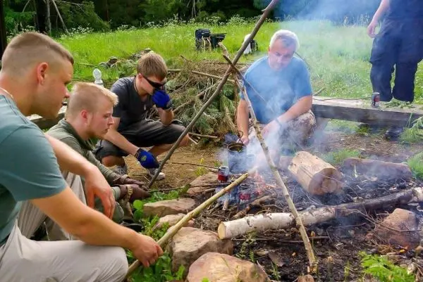 Kleine Flamme raucht zwischen Holzstücken, Teilnehmer sitzen im Kreis darum