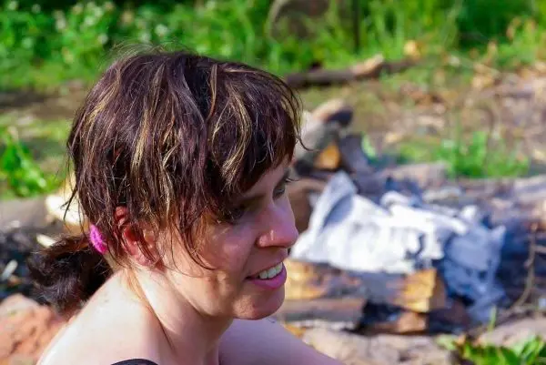 Kleines Bodenfeuer mit Holzscheiten im Hintergrund, Person sitzt daneben