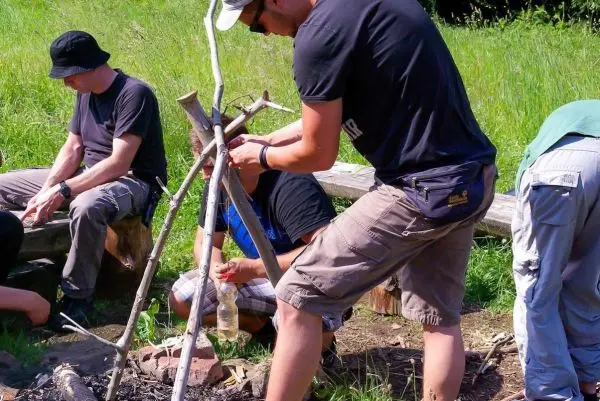 Mann baut eine improvisierte Kochstelle mit Holzstücken und Schnur