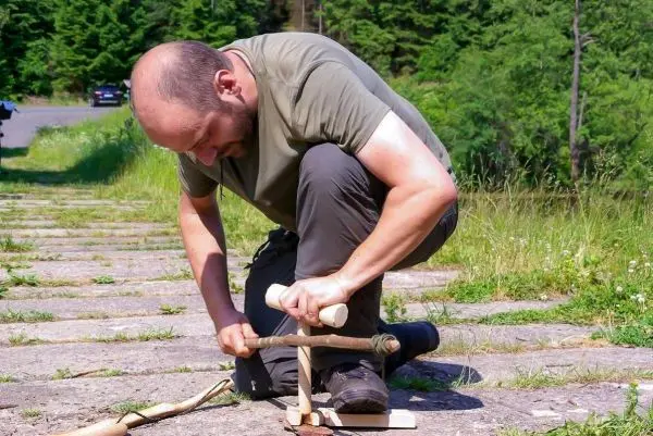 Mann bearbeitet Holzstück mit einem improvisierten Feuerbohrer