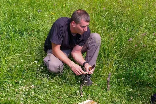 Mann bearbeitet Holzstück mit einem Messer im hohen Gras