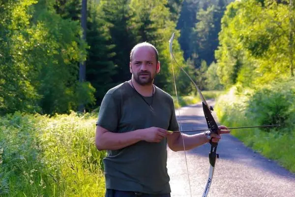 Mann hält einen Bogen und Pfeil auf einem Waldweg