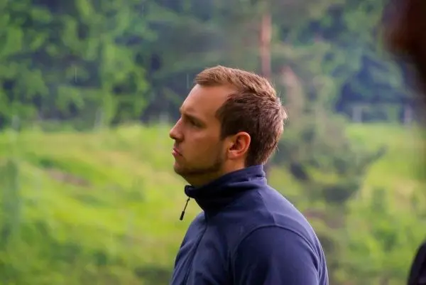 Mann mit dunklem Pullover steht in der Natur und schaut nach oben