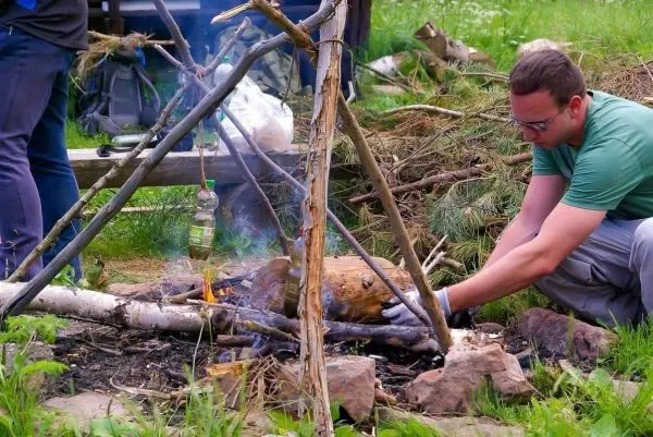 Mann platziert einen Kessel über einem kleinen Feuer unter einem Dreibein