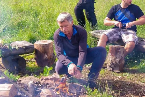 Mann sitzt am Bodenfeuer und hält einen Topf über die Flamme