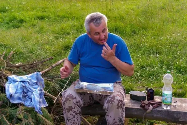 Mann sitzt auf einer Bank, hält ein Tablett mit Essen und gestikuliert