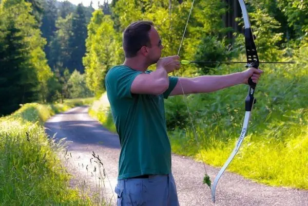 Mann spannt einen Bogen auf einem Waldweg
