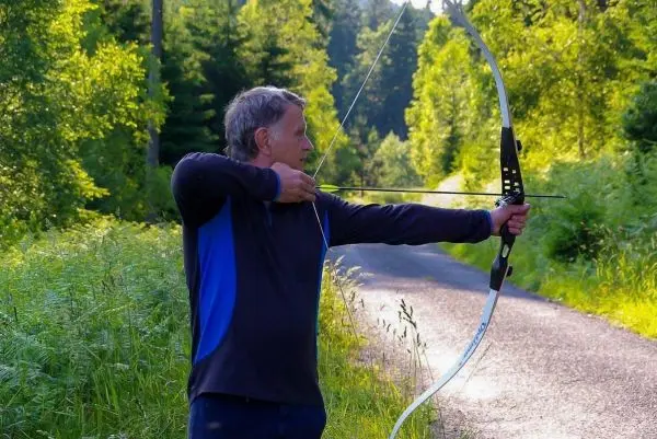 Mann spannt einen Bogen auf einem Waldweg
