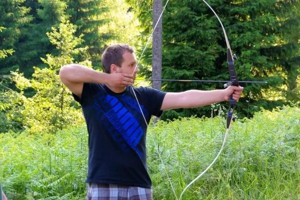 Mann spannt einen Bogen im Wald und zielt auf ein Ziel