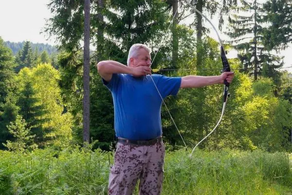 Mann spannt einen Bogen im Wald und zielt auf ein Ziel