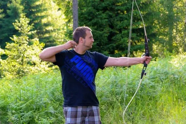 Mann spannt einen Bogen in einer bewaldeten Umgebung