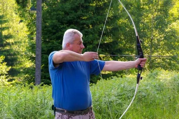 Mann spannt einen Bogen in einer bewaldeten Umgebung