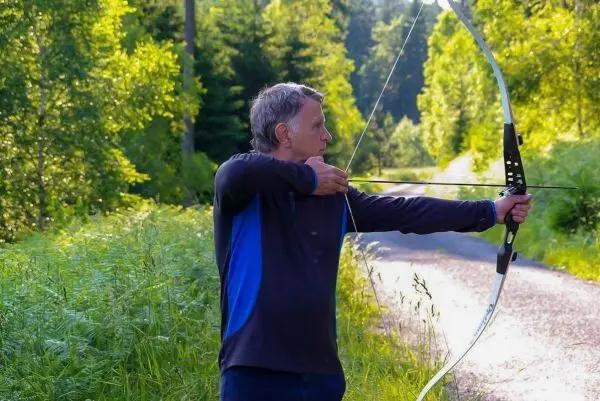 Mann spannt einen Bogen in einer bewaldeten Umgebung