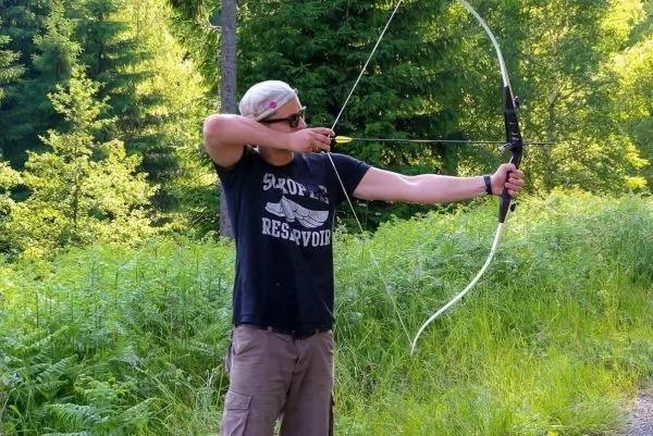 Mann spannt einen Bogen in einer Waldlandschaft