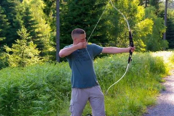 Mann spannt einen Bogen in einer Waldlandschaft