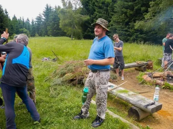 Mann steht in der Natur, umgeben von anderen Personen und Holzmaterialien